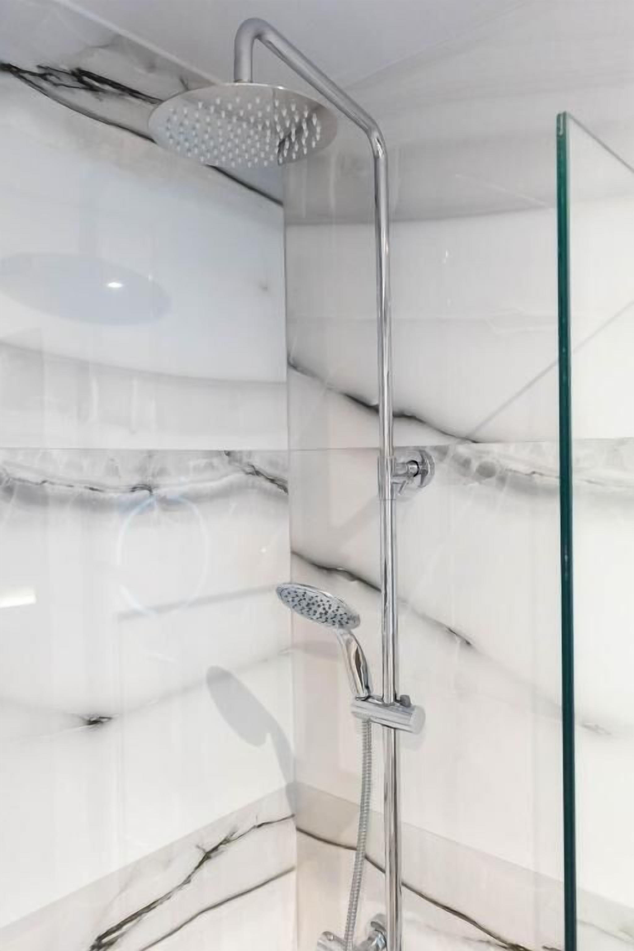 Un baño moderno con cabina de ducha de vidrio, baldosas de mármol y separador de vidrio.