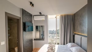 Egy modern szállodaszoba, amelyben egy nagy ágy, egy falra szerelt, síkképernyős televízió található, és az ablakon keresztül a városra nyílik kilátás.