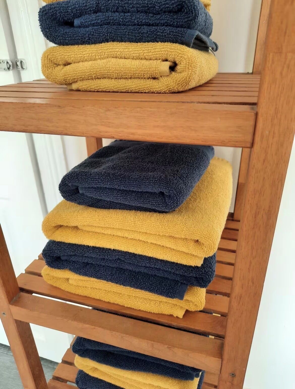 Uno scaffale di legno con asciugamani piegati nei colori blu e senape.