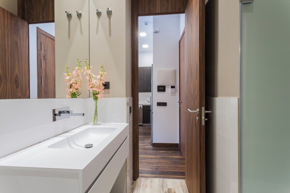 A modern bathroom with a white sink, wooden vanity, and a mirror. There is a vase with flowers on the vanity. - Dobo Madrid Gran Vía (Madrid)