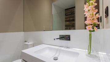 Un baño moderno con un lavabo blanco, un espejo y un florero con flores rosadas.
