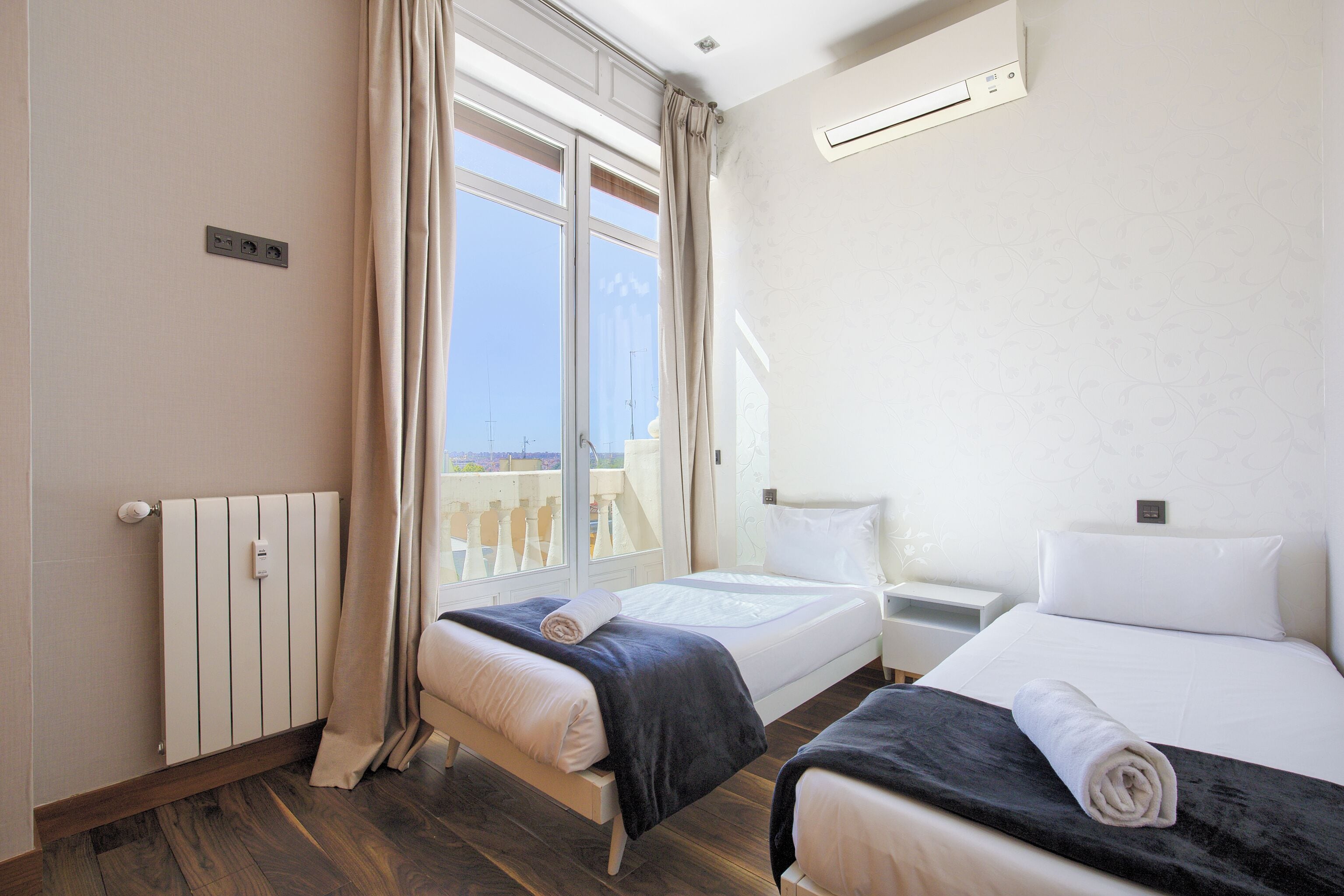 Une chambre d’hôtel avec deux lits, une fenêtre avec des rideaux, un radiateur et une petite table de chevet.
