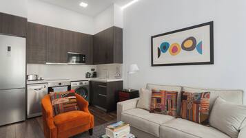 Una cocina moderna con armarios de madera oscura, un microondas y una cafetera. Hay un sofá con almohadones coloridos y un cuadro abstracto enmarcado en la pared.