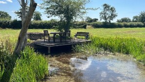 A wooden deck with a table and benches overlooking a body of water. - Cotswolds Country Cottage | Boutique, Romantic Retreat for Two (Purton Stoke)