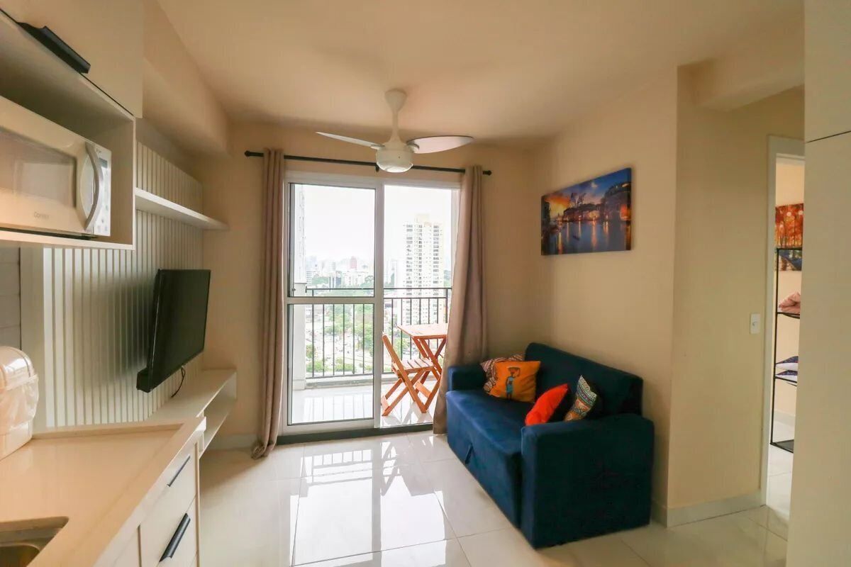 Ein modernes Wohnzimmer mit Flachbildfernseher, Deckenventilator, einer Couch mit Kissen, einem Esstisch und einem Balkon mit Blick auf die Stadt.