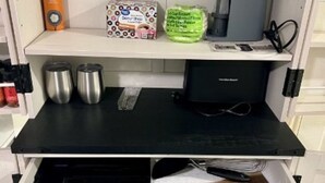 Un coin cuisine avec un plan de travail noir, une machine à café, une boîte de capsules de café, un sac de farine et deux récipients en acier inoxydable.