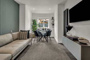 A modern living room with a sofa, dining table, chairs, and a TV mounted on the wall. - Stanley Park House, Peterborough - 3 bedroom, 3 bathroom, parking, City centre (Peterborough)