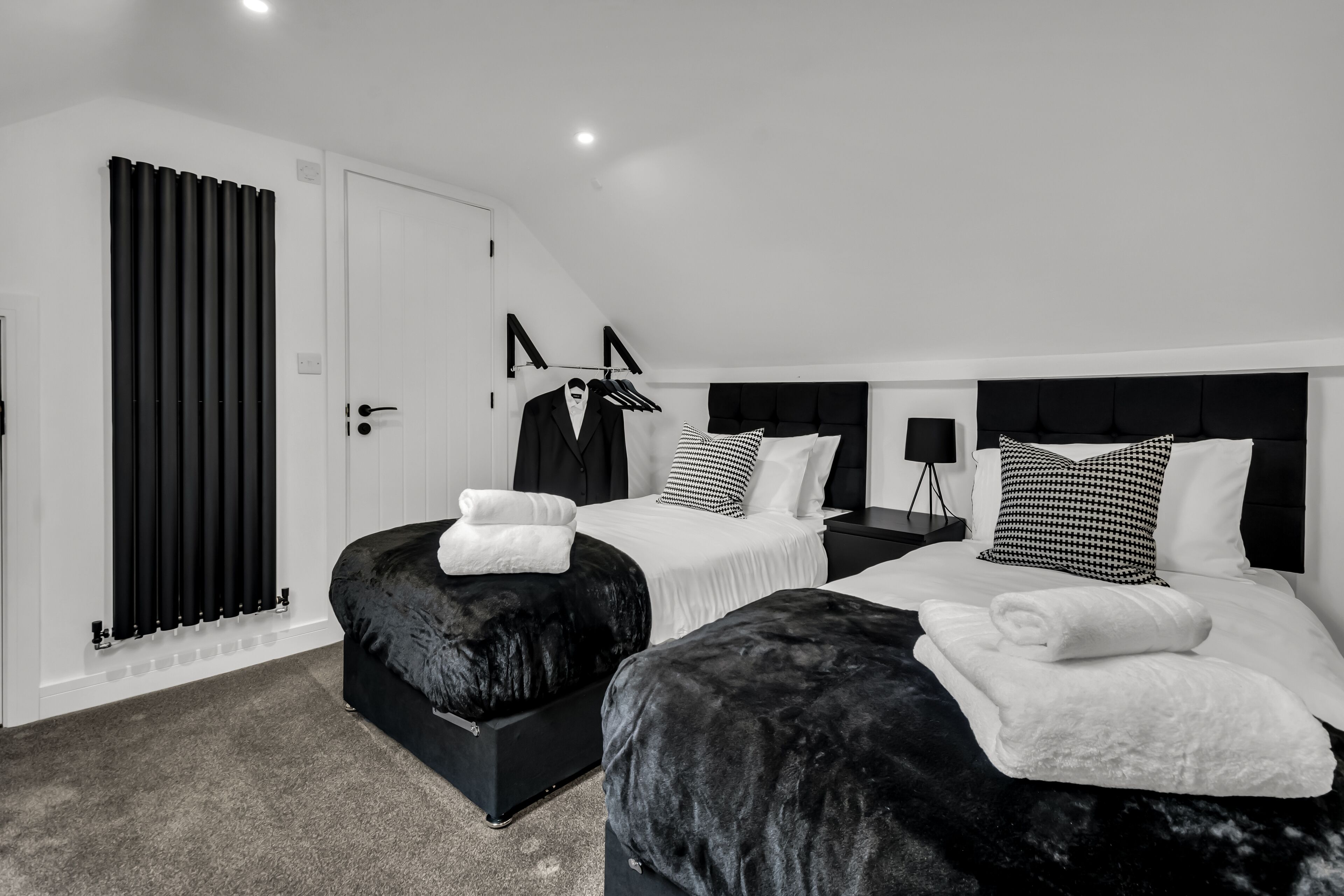 A modern hotel room with two beds, a black and white color scheme, and a black radiator.