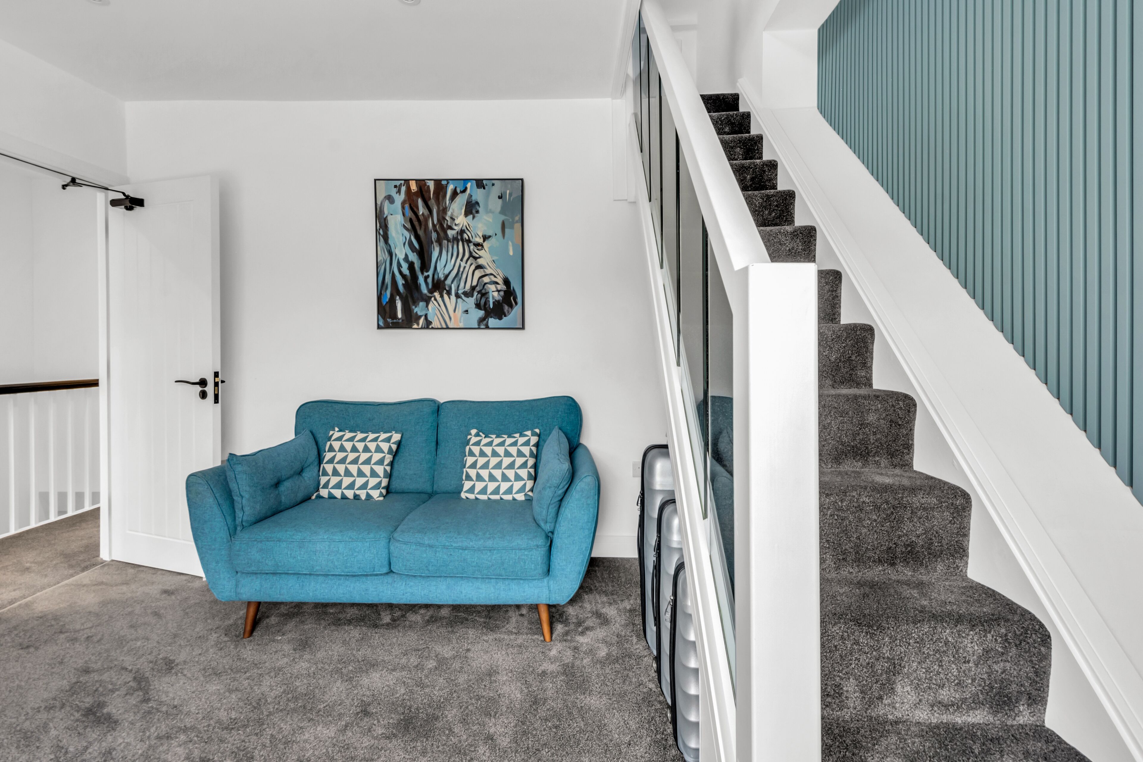 En moderne stue med en turkis sofa, et zebra maleri og en trappe med hvide gelændere.