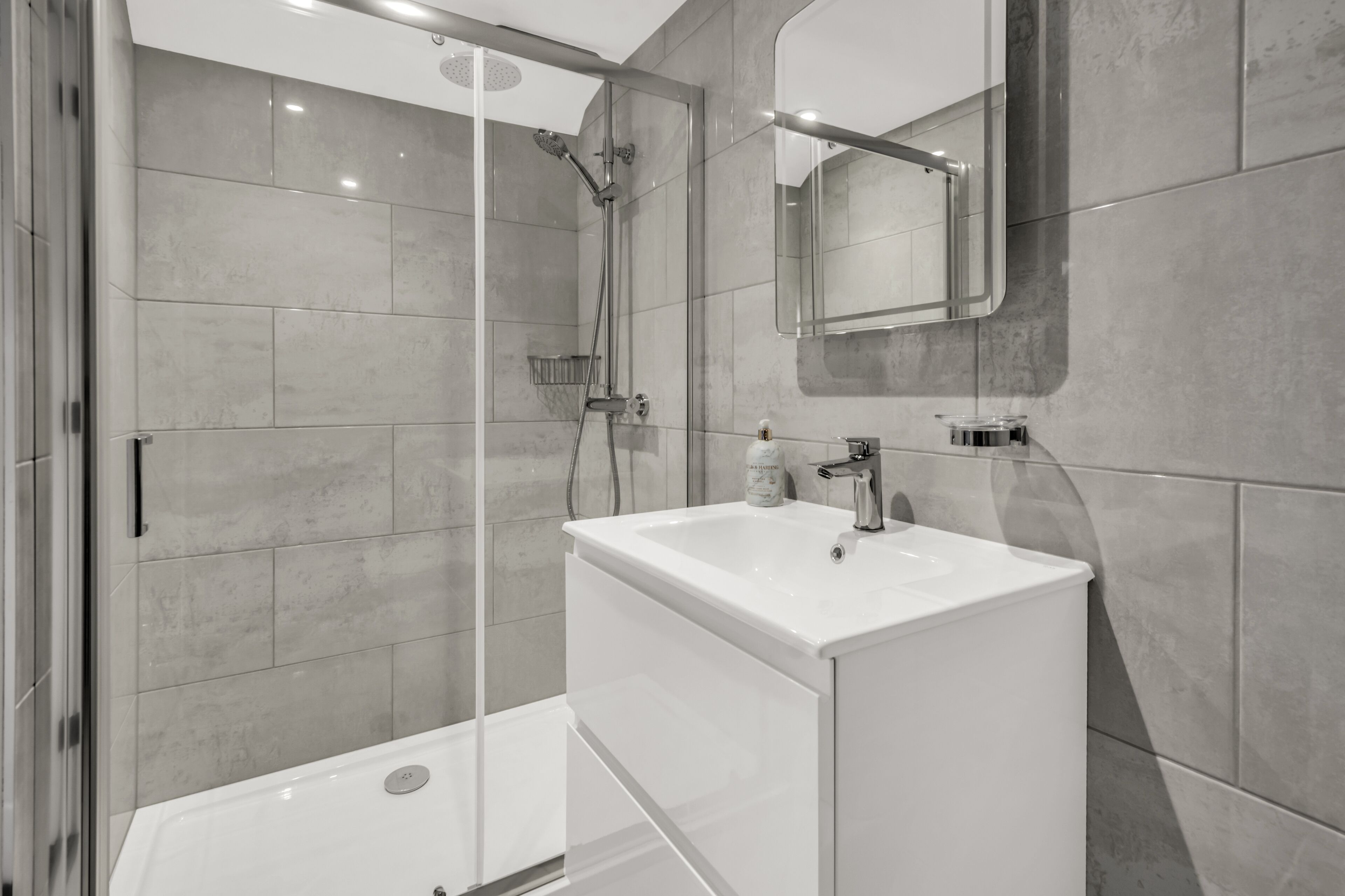 A modern bathroom with a glass-enclosed shower, a white sink, and a large mirror.