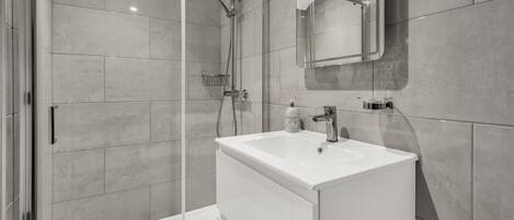 A modern bathroom with a glass-enclosed shower, a white sink, and a large mirror.