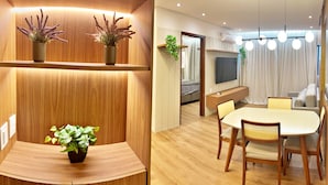 A modern living room with a wooden accent wall, a dining area with a round table and chairs, and a TV mounted on the wall. - Vacanze - Infiniti (Maceió)