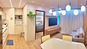Ett modernt hotellrum med ett litet kök, en säng med utsikt, en TV, en sittgrupp och ett matbord.