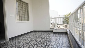 Un balcon avec des carreaux de sol à motifs, une fenêtre ornée de barreaux et une vue sur un chantier de construction.