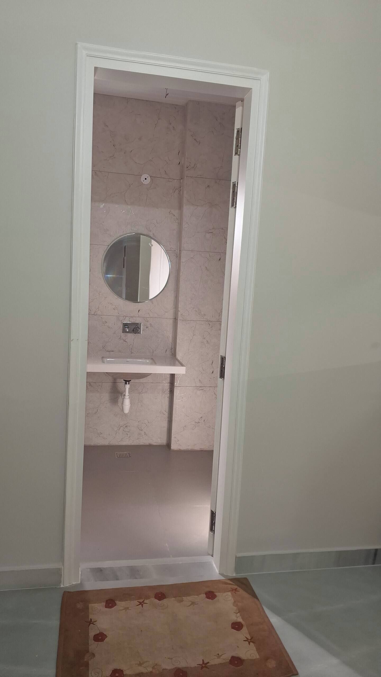 Une salle de bain avec un mur en marbre, un miroir rond et un lavabo blanc.