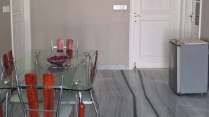 Un comedor con mesa y sillas de vidrio, un refrigerador y una puerta.