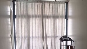 Un comedor con una mesa y sillas, una caminadora y un ventanal con cortinas translúcidas.