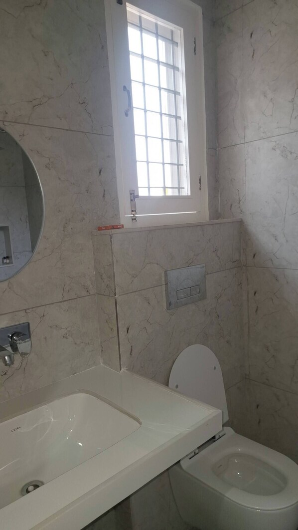 Une salle de bain avec un lavabo blanc, des toilettes, une fenêtre avec des stores et un miroir.