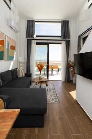 Un soggiorno moderno con divano, televisore e vista su un balcone con sedute all'aperto.