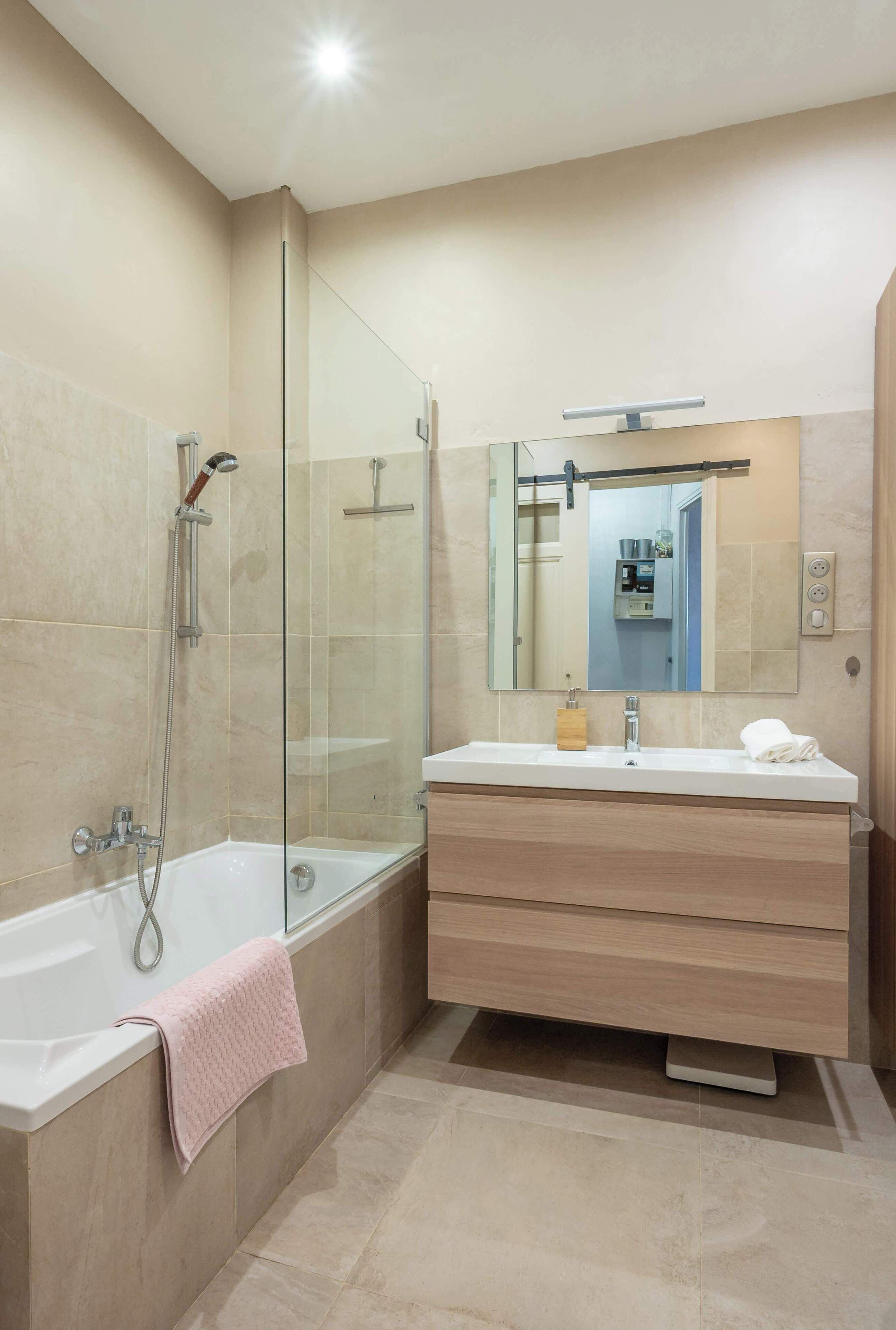A modern bathroom with a glass-enclosed shower, a white bathtub, and a vanity with a mirror.