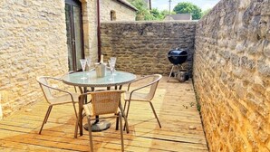 Een houten terras met een ronde tafel en stoelen, een barbecue en een stenen muur.