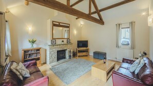 Een ruime woonkamer met een stenen open haard, houten balken, een televisie en leren banken.
