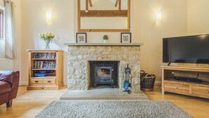 Een woonkamer met een stenen openhaard, een houten bovenblad, een televisie op een houten dressoir en een boekenkast.