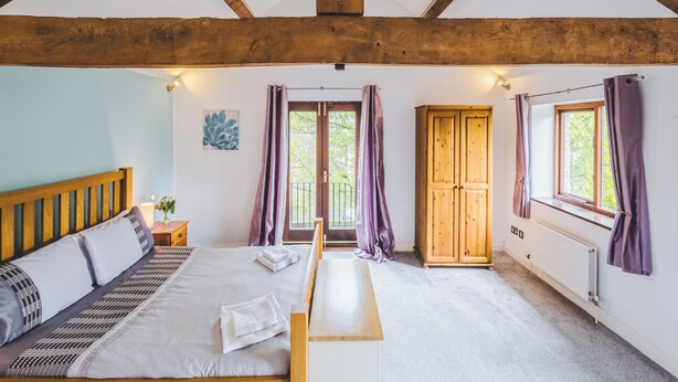 Een slaapkamer met een houten bed, een nachtkastje met een lamp, een bankje en een kledingkast.