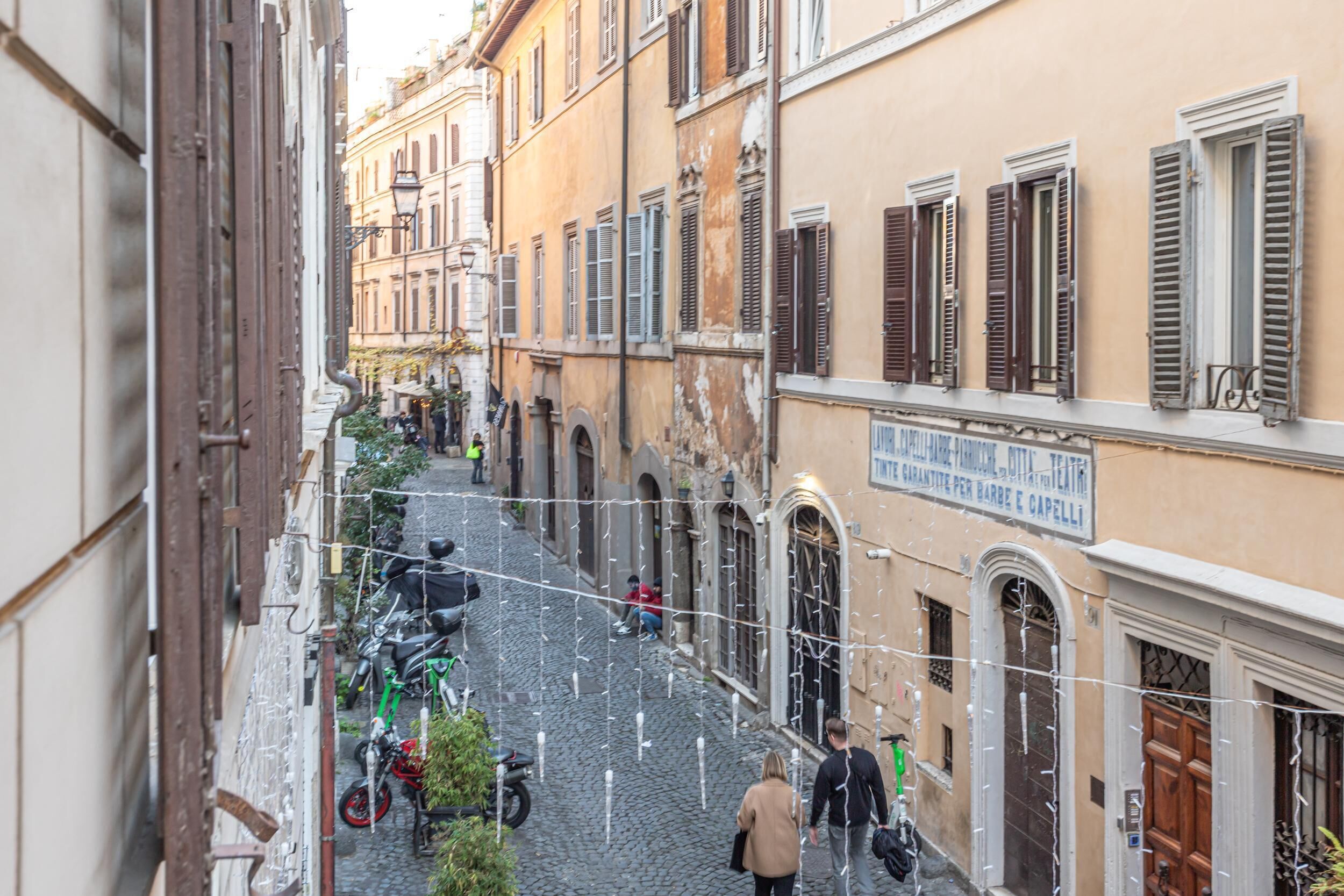Un vicolo stretto con pavimentazione in pietra ciottolata, edifici storici con portali ad arco e un'insegna per un bar e un ristorante.