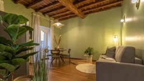 A living room with a sofa, a dining table with chairs, a potted plant, and a wooden ceiling. - Giada   Charming Apartment at the Imperial Forums (ROMA)