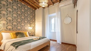 A bedroom with a wooden bed, patterned wallpaper, a window with curtains, and a decorative wall hanging. - Giada   Charming Apartment at the Imperial Forums (ROMA)
