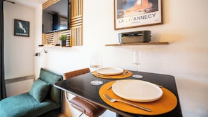A dining area with a table set for two, a television mounted on a wooden panel, and a poster of Lac d'Annecy. - Thank you Annecy - Near Lake (Annecy)