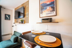 A dining area with a table set for two, a television mounted on a wooden panel, and a poster of Lac d'Annecy. - Thank you Annecy - Near Lake (Annecy)