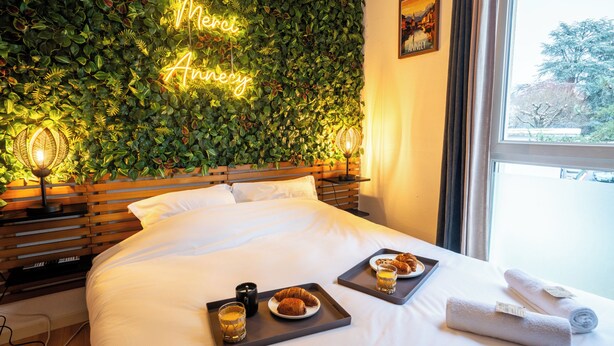 A hotel room with a bed, a neon sign on the wall, and breakfast trays on the bed. - Thank you Annecy - Near Lake (Annecy)