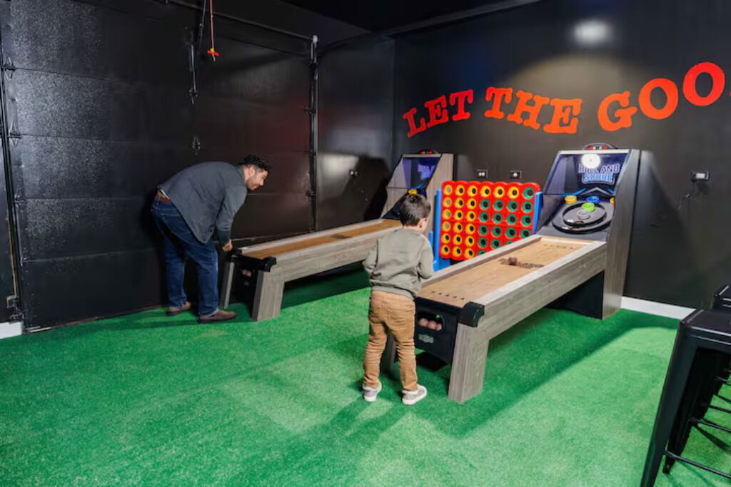 Ein Zimmer mit Teppich in Grün, einem Holztisch und zwei Spielautomaten.