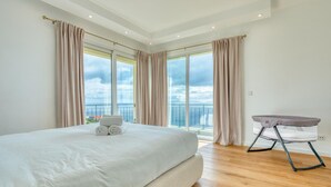 Une chambre spacieuse avec un grand lit, un balcon avec vue et un berceau pour bébé.