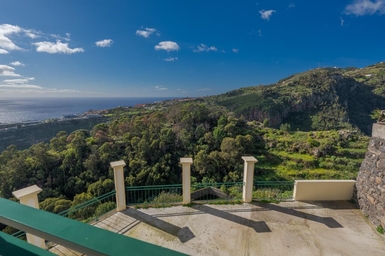 A balcony with a view of a coastal landscape, including a forested hill and the ocean.