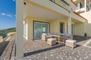 Eine überdachte Terrasse im Freien mit Esstisch, Korbmöbeln und Blick auf die Landschaft.