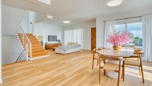 Un vaste espace de vie agrémenté d’un escalier en bois, d’une table à manger avec des chaises, d’un canapé et d’une grande fenêtre avec des rideaux.