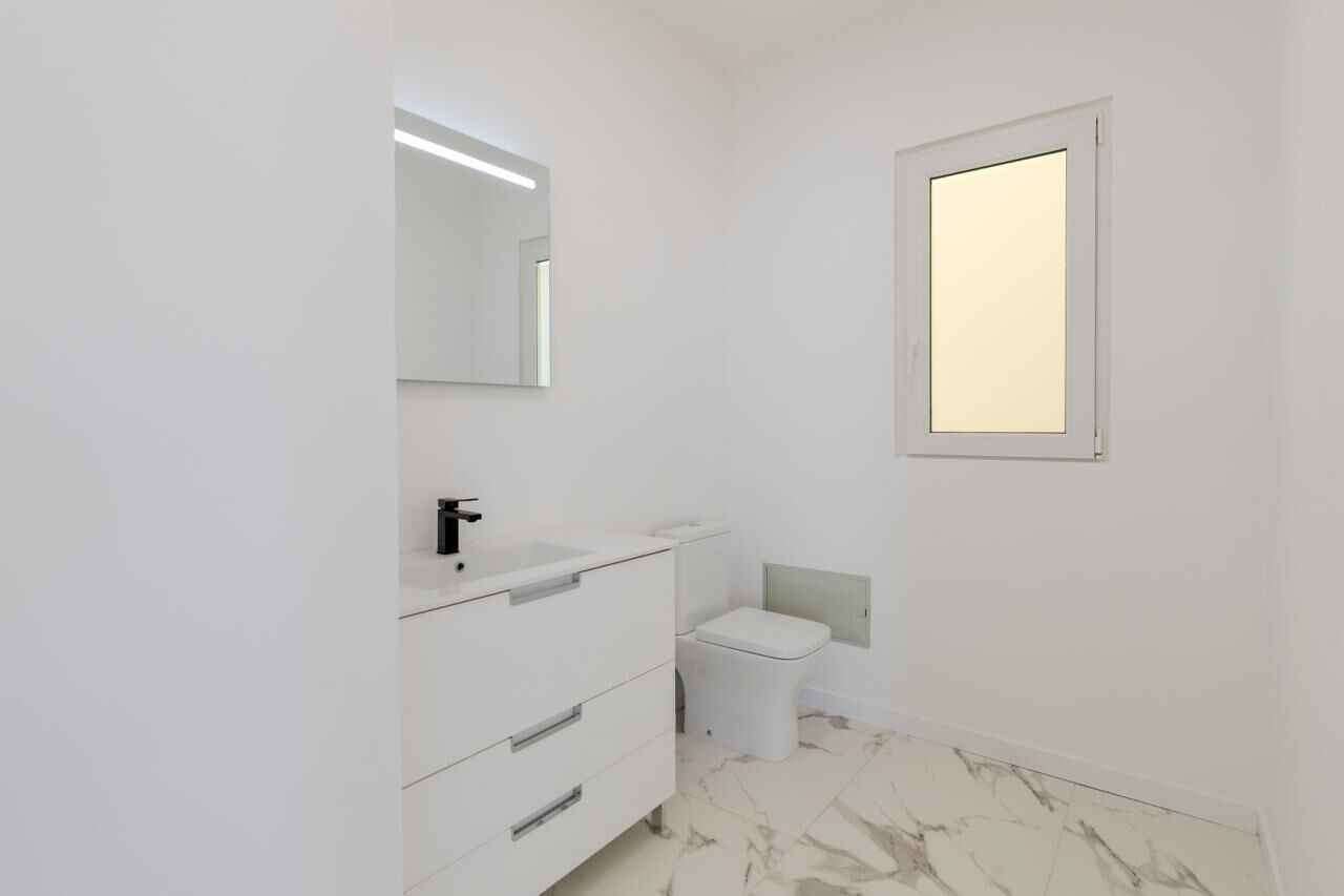 A small, clean bathroom with a white sink, a mirror, and a toilet.