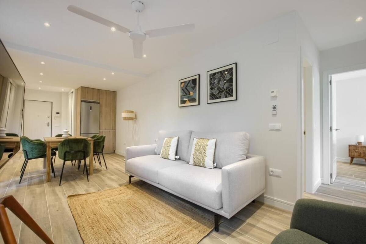 Ein modernes Wohnzimmer mit einem weißen Sofa, grünen Sesseln, einem Esstisch und einem Deckenventilator.