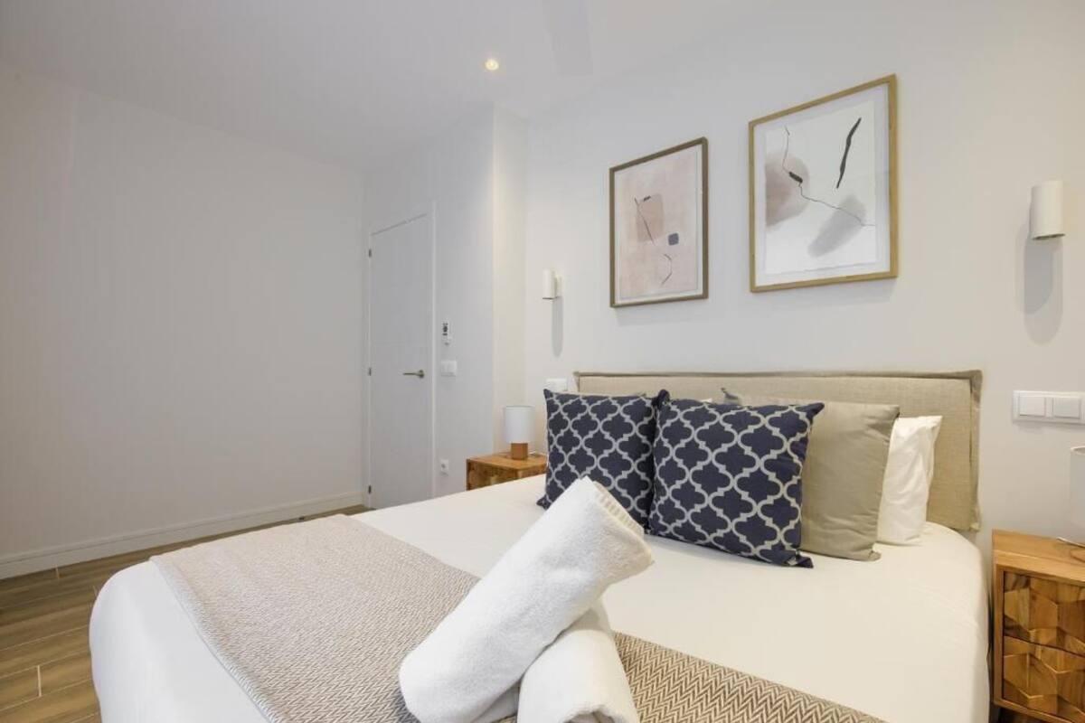 Ein ordentlich eingerichtetes Hotelzimmer mit Bett, Kissen, Nachttisch und Wandbildern.