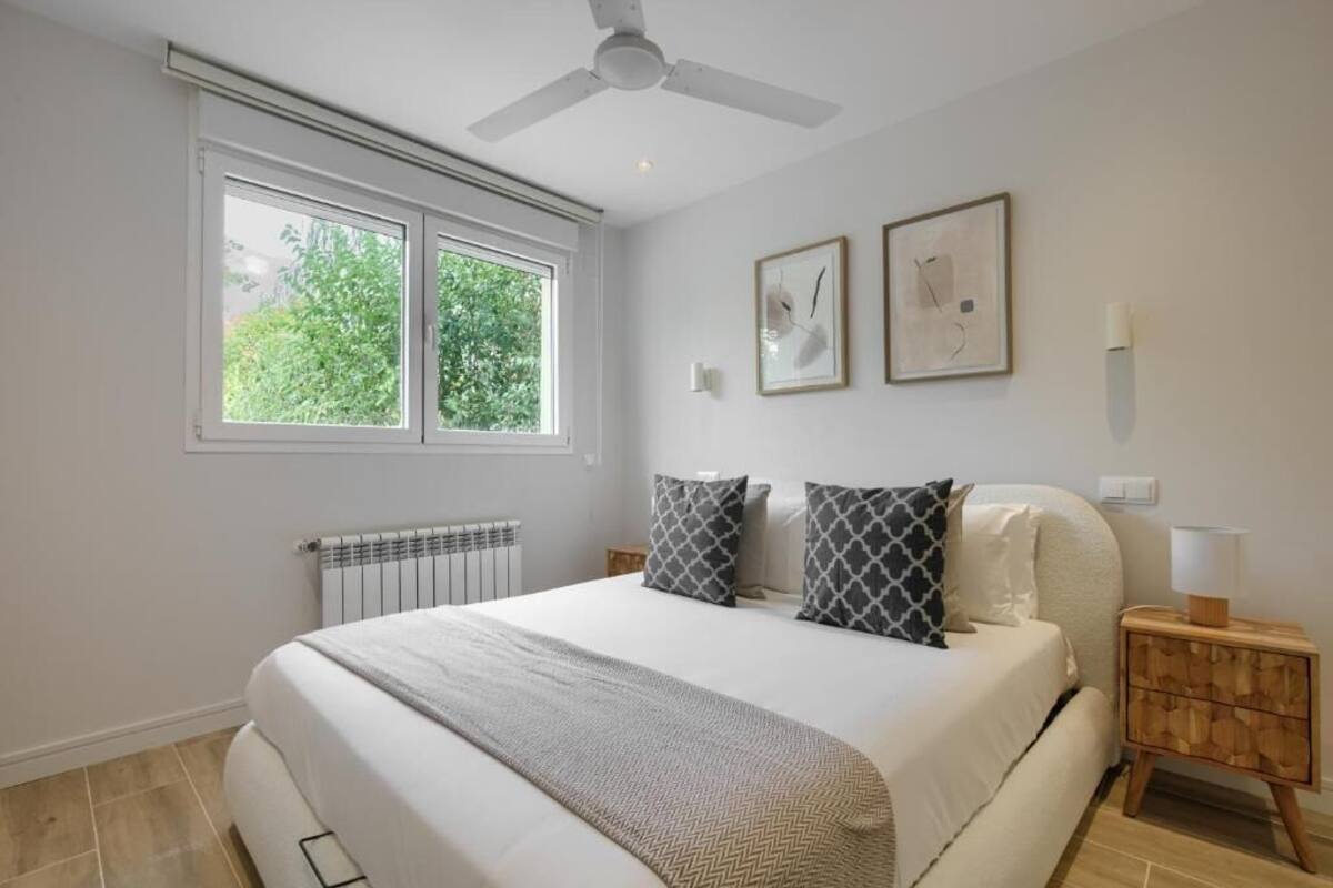 Ein Schlafzimmer mit einem Bett, zwei Nachttischen, einem Deckenventilator, einem Fenster und zwei gerahmten Bildern an der Wand.