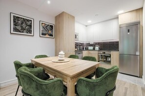 Eine moderne Küche mit einem Holztisch und grünen Stühlen, einem Kühlschrank und einer Mikrowelle.