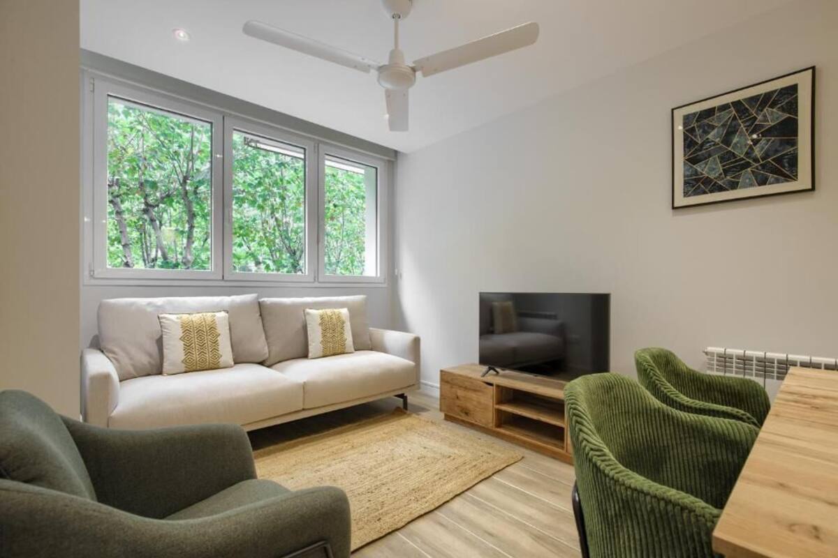 Ein modernes Wohnzimmer mit einer Couch, einem Fernseher und grünen Sesseln.