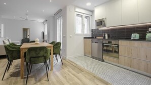 A modern kitchen with wooden cabinets, a microwave, and a dishwasher. There is a dining area with a wooden table and green chairs. - Dobo Madrid Pinar Aptos Temporales (Madrid)