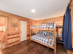 A bunk bed with a checkered bedspread, a white door, and a wall-mounted decorative item. - Pet-Friendly  Mountain Cabin | Hot Tub & Fire Pit (Sautee Nacoochee)