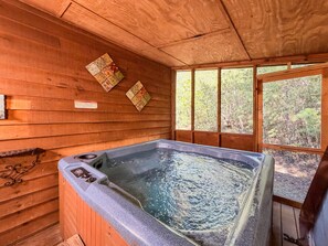 A wooden cabin with a hot tub, wooden walls, and a window with a forest view. - Pet-Friendly  Mountain Cabin | Hot Tub & Fire Pit (Sautee Nacoochee)