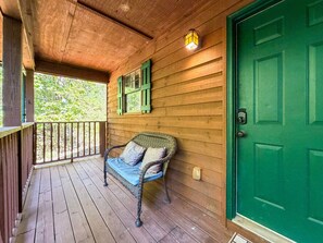 A wooden porch with a green door, a wicker chair with cushions, and a window with green shutters. - Pet-Friendly  Mountain Cabin | Hot Tub & Fire Pit (Sautee Nacoochee)