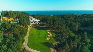 Vista aérea de un campo de golf con un club de campo y una casa grande rodeada de bosque denso.
